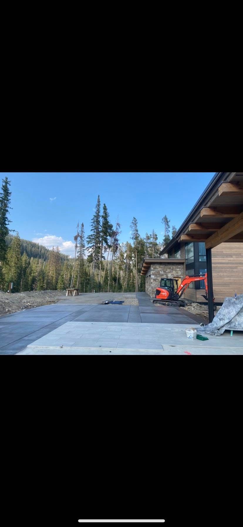 Outdoor concrete patio beside a cabin, with an orange tractor and pine trees under a clear sky.