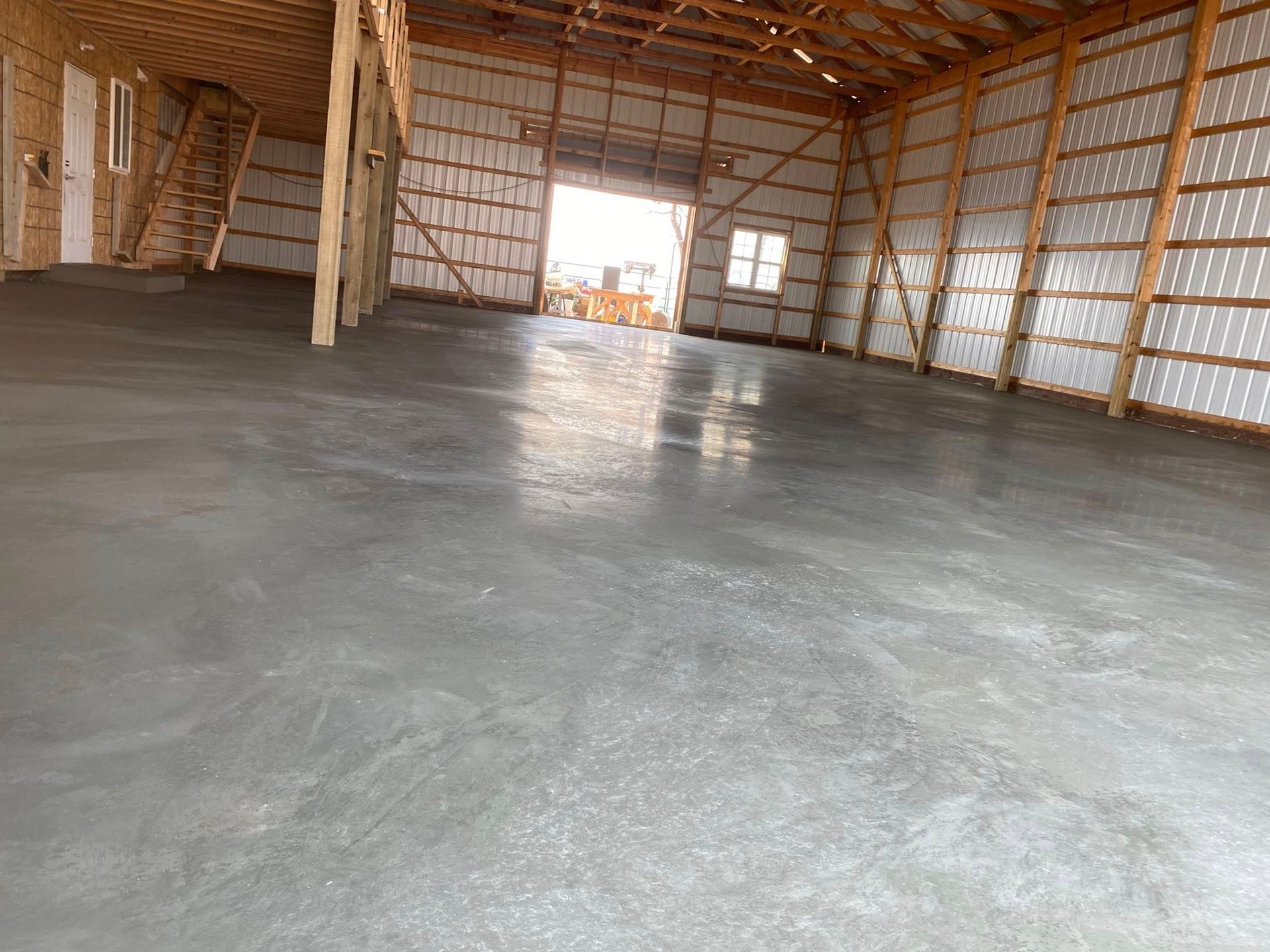 Empty warehouse interior with a polished concrete floor, exposed wood framing, and open doorway at the far end