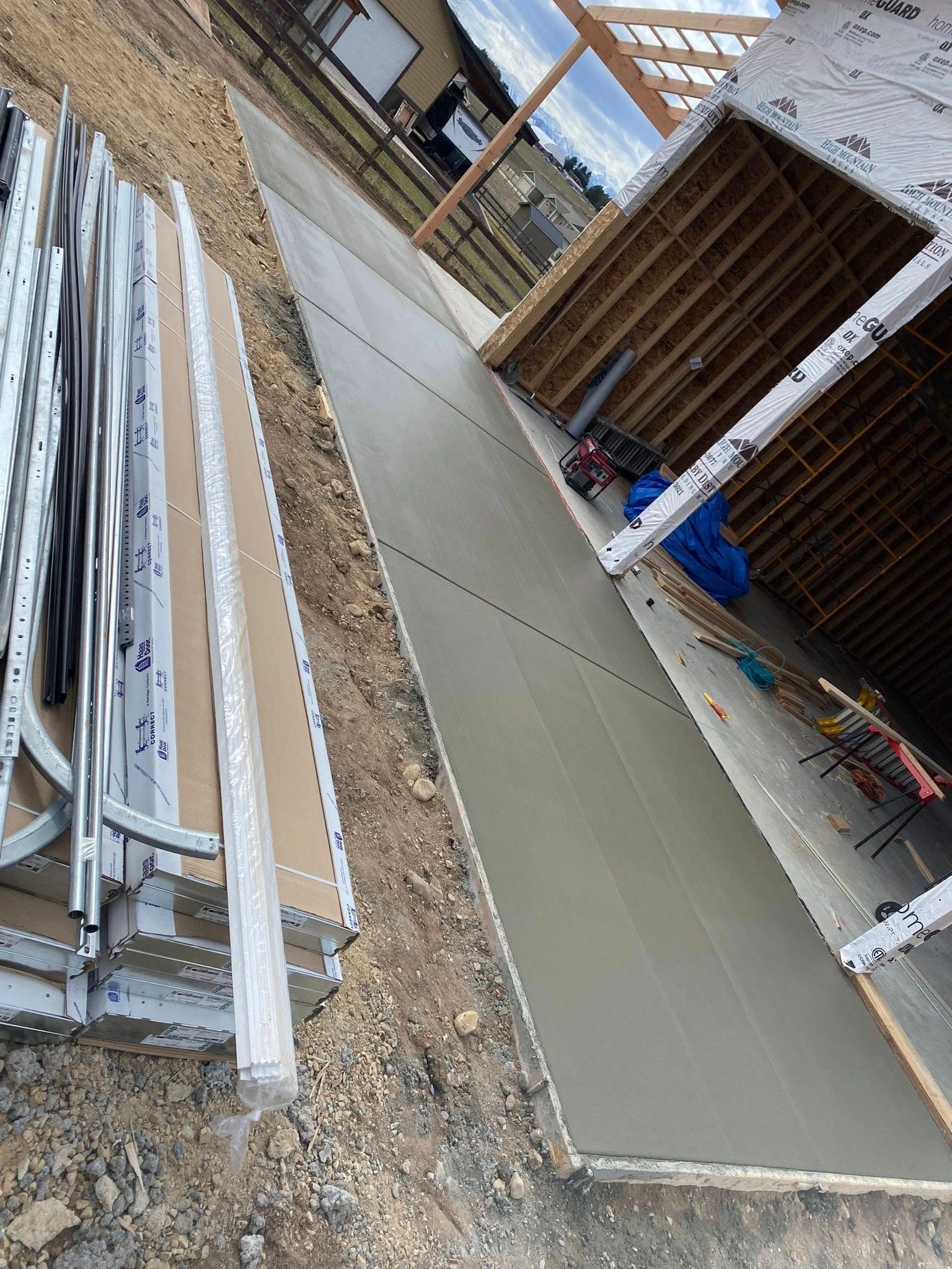 Construction site with freshly poured concrete walkway beside stacked metal rails and materials
