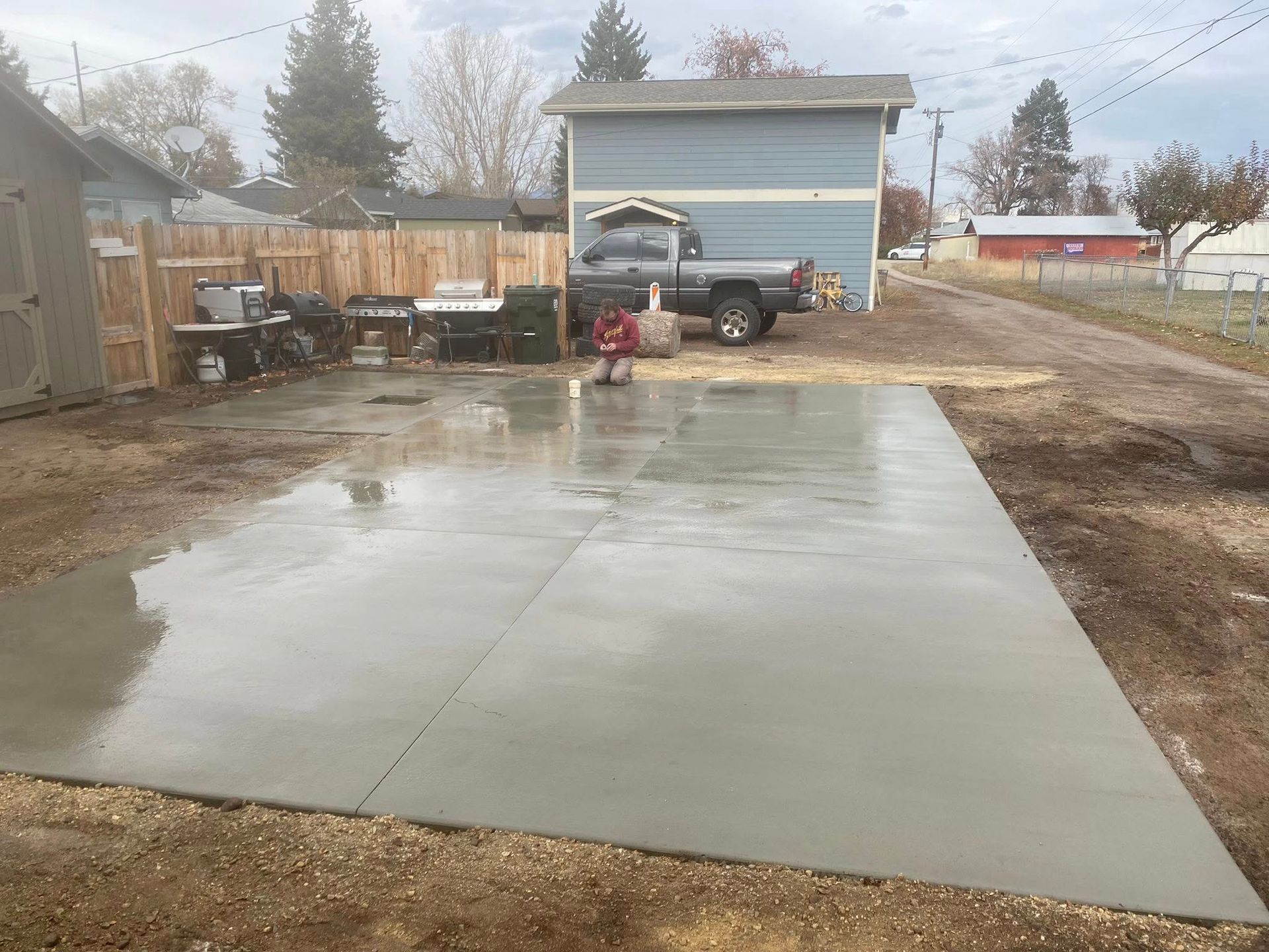 Fresh concrete driveway in a backyard, with a truck and small shed in the background