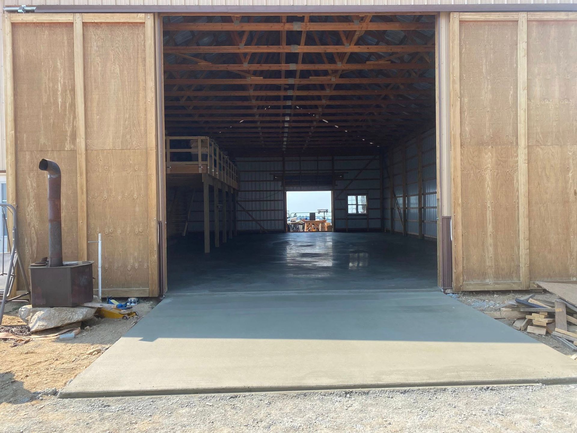 Open warehouse bay with concrete floor and large sliding wooden doors, view through to back opening.