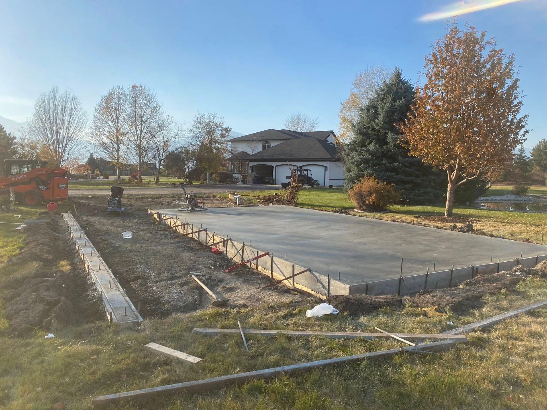 Raised concrete patio foundation in a yard, with a house and autumn trees in the background.