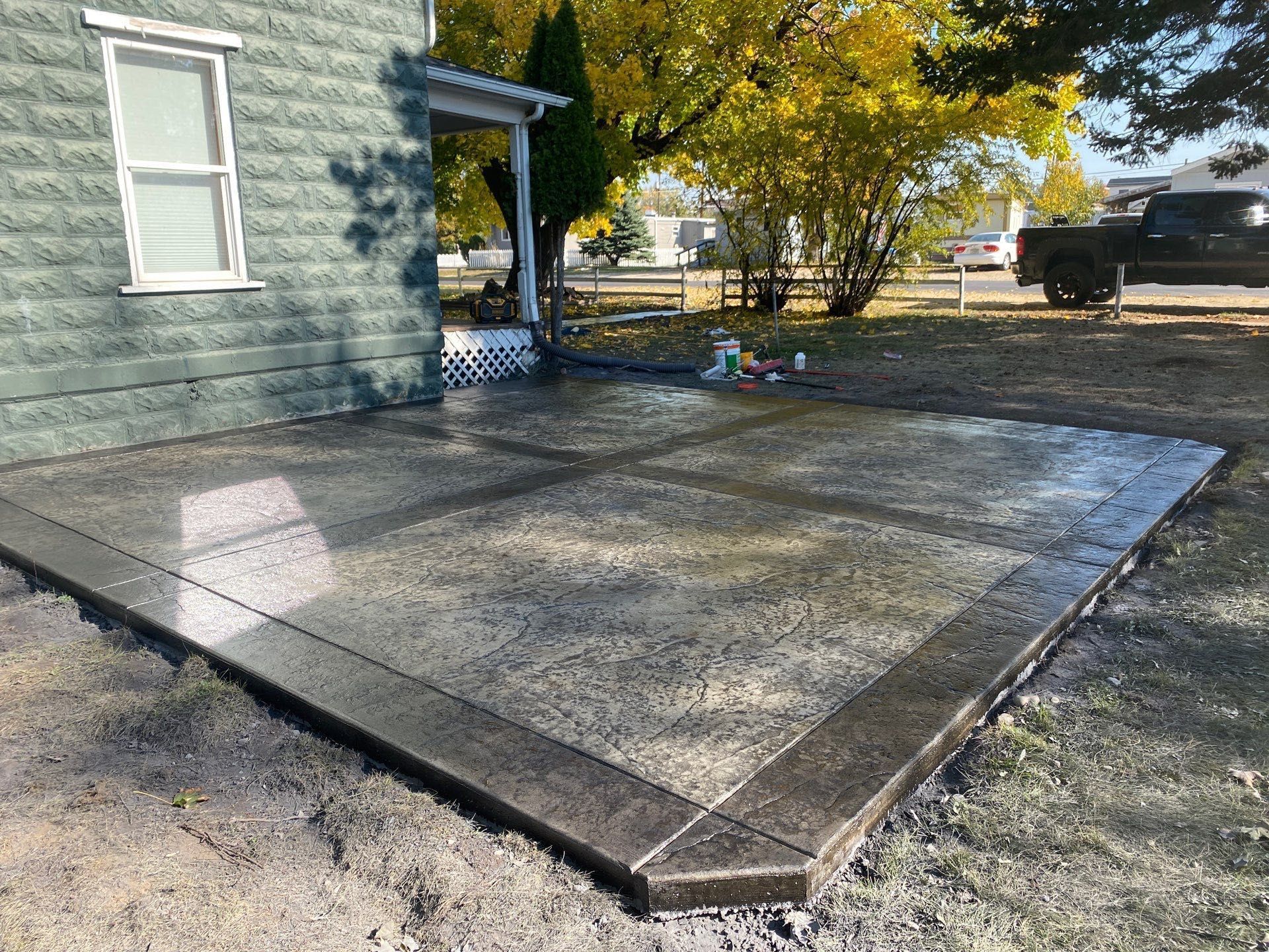 Concrete patio beside a blue house with a covered porch and trees in the background