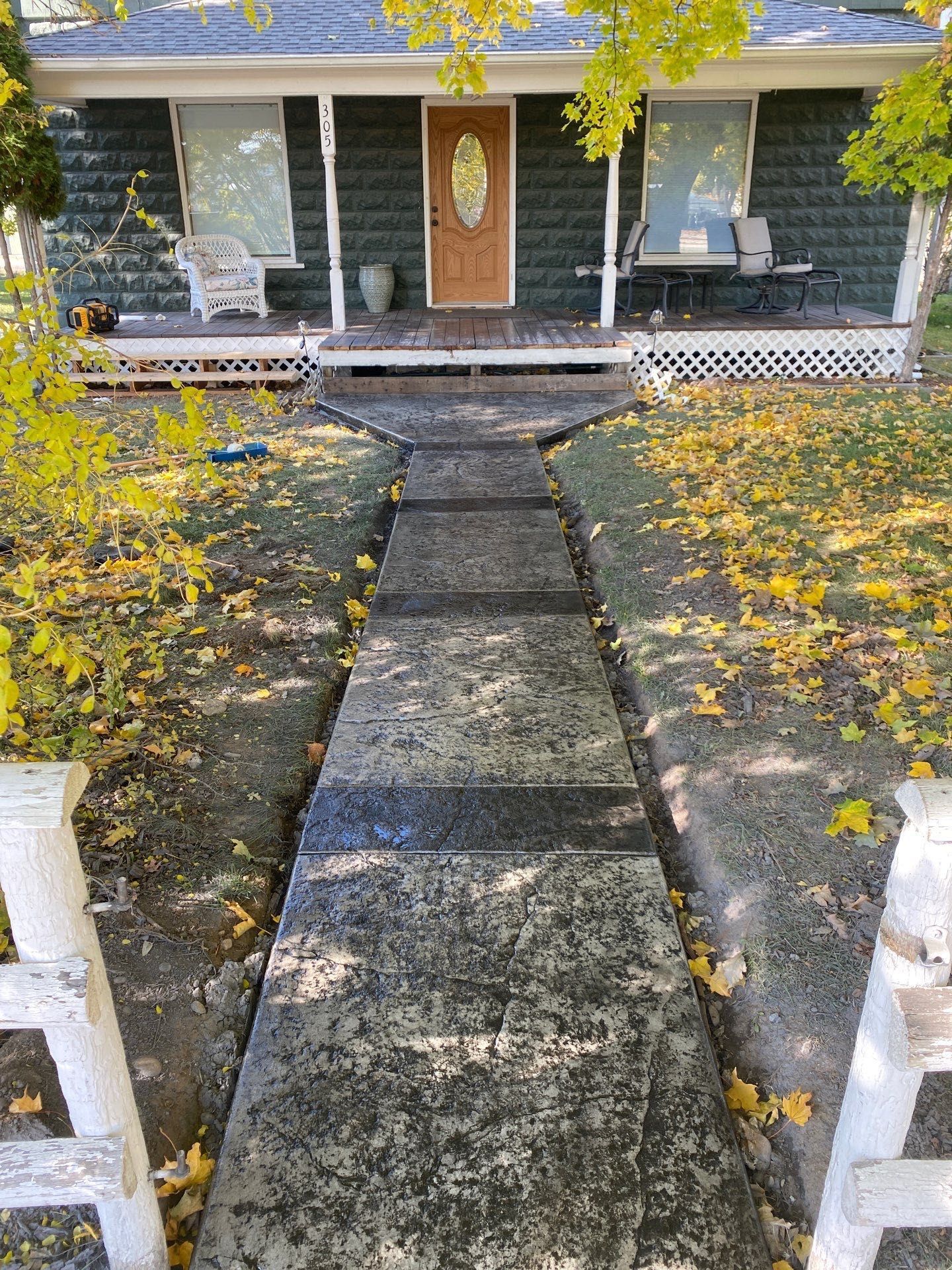 Front walkway leading to a gray house with an orange door, lined with white posts and scattered autumn leaves.