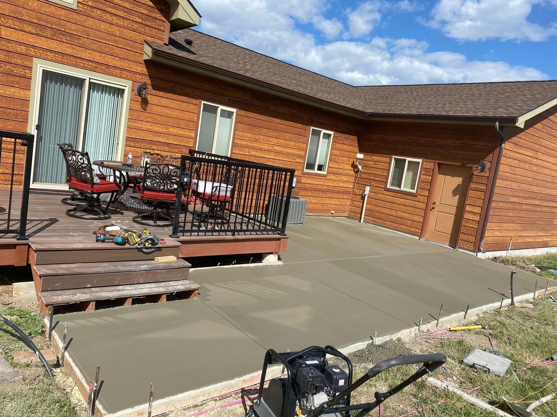 Backyard patio with concrete slab, wooden deck, red-brick house, and patio furniture in sunlight