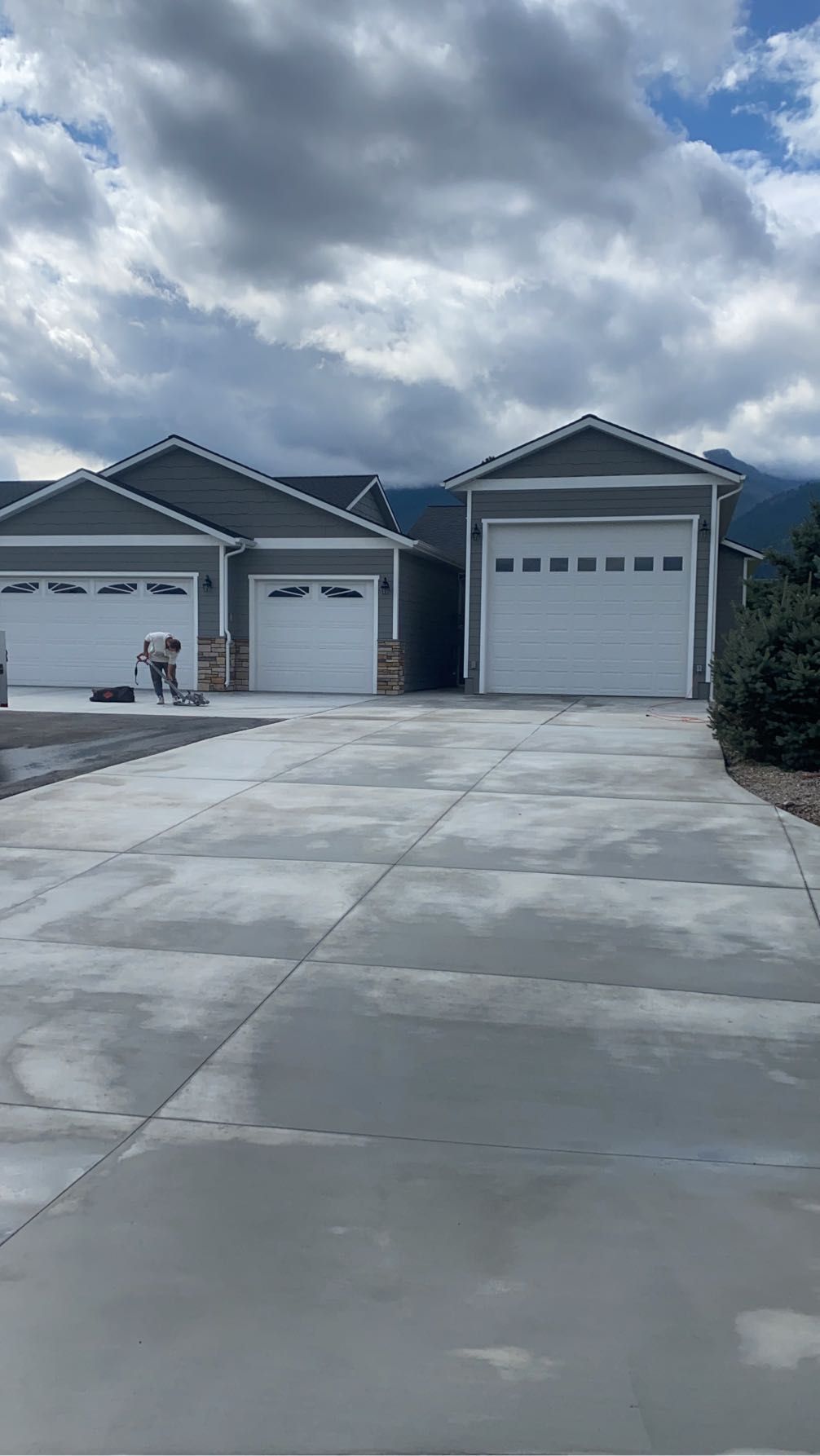 Suburban driveway leading to two gray single-story garages under a cloudy sky