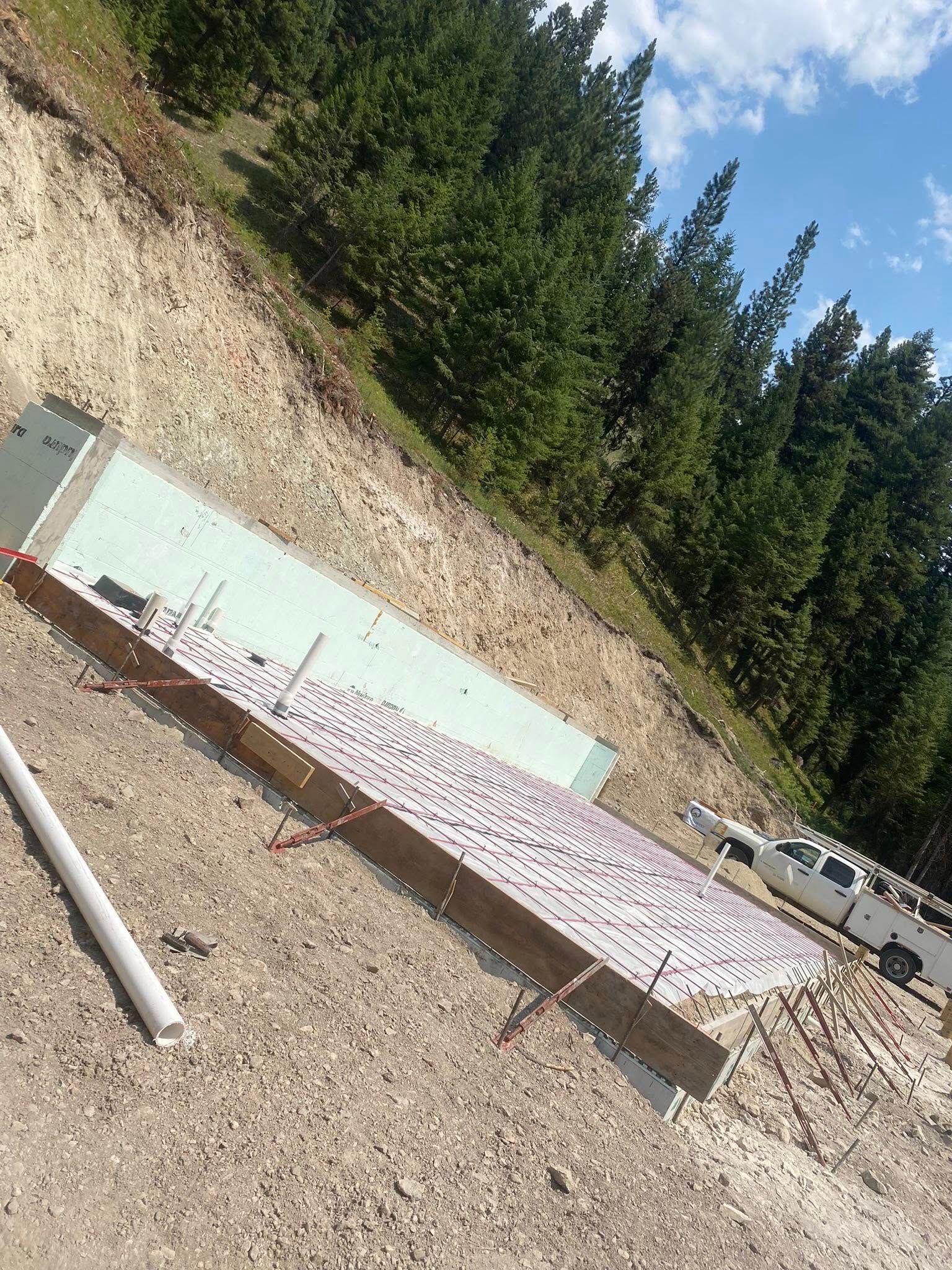 Outdoor gravel lot with a tilted white sign and dense evergreen trees under a blue sky
