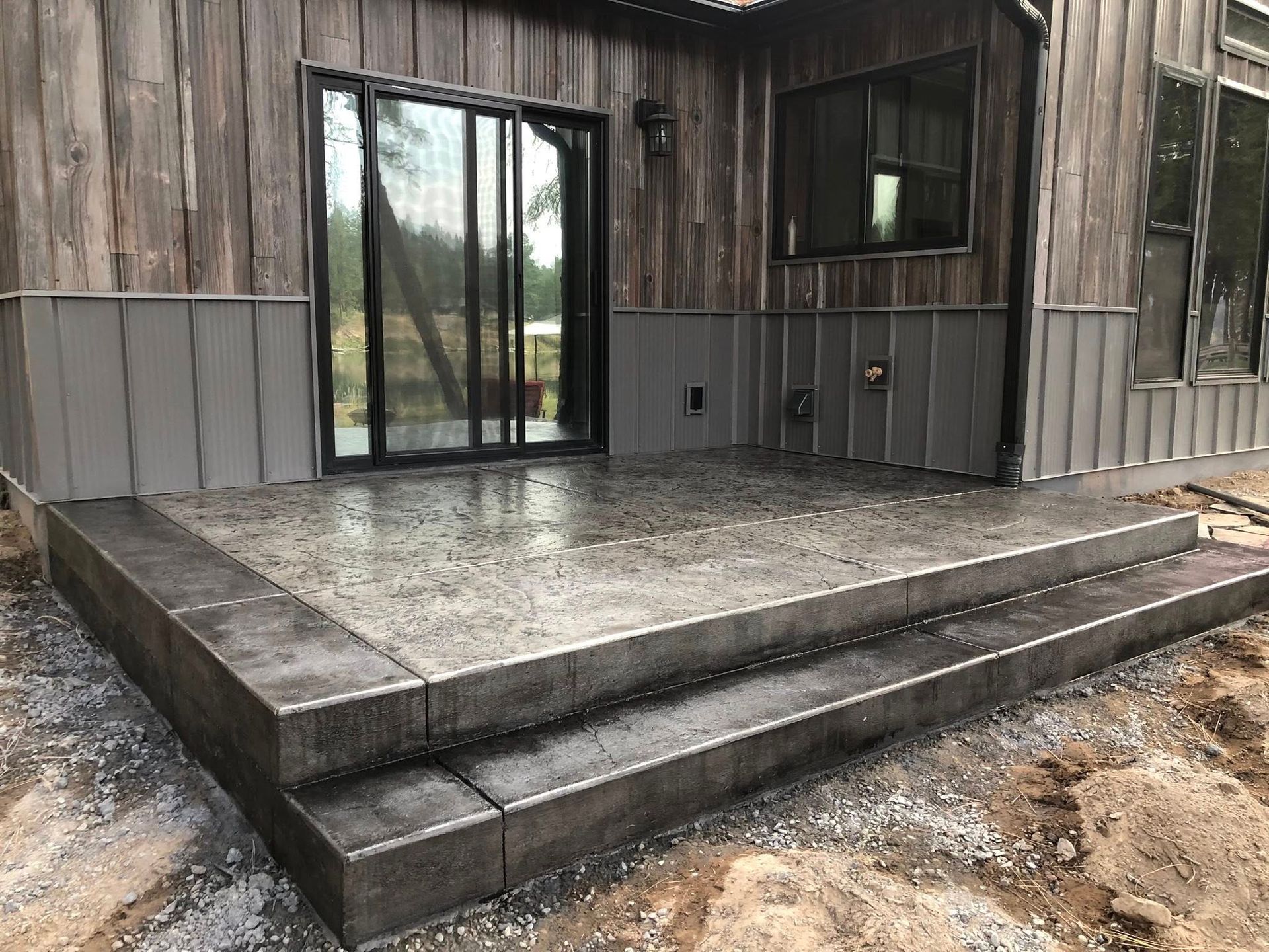 Covered wooden patio with two concrete steps and sliding glass doors on a rustic building