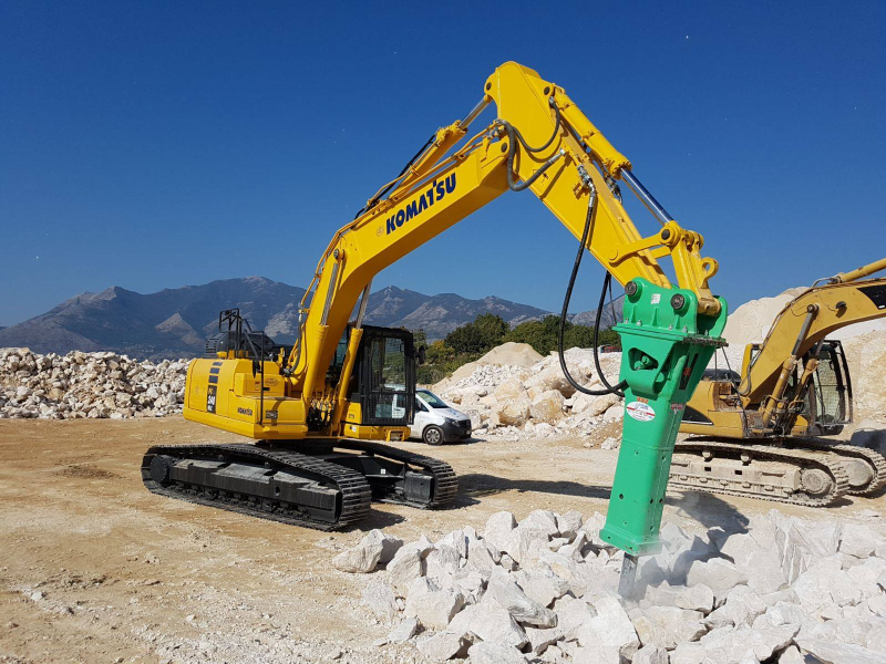 Un camion con un braccio meccanico carica rottami metallici nel suo container sotto un cielo azzurro.