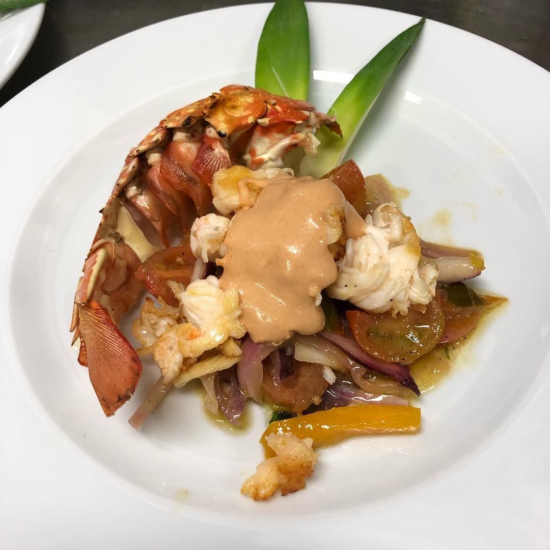 Un piatto bianco sormontato da una coda di aragosta e verdure