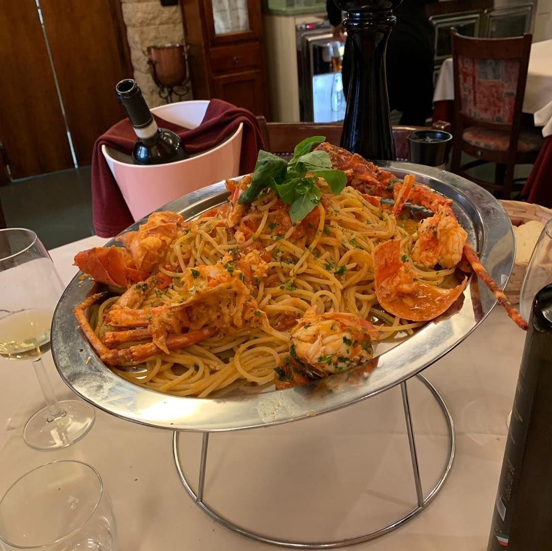 Un piatto di spaghetti con gamberi e una bottiglia di vino su un tavolo.