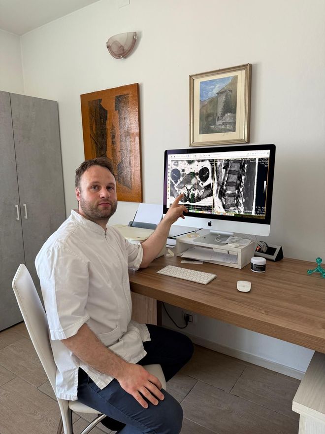 Man pointing at a computer screen displaying an x-ray, sitting at a desk in an office.