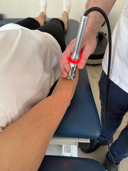 Person receiving laser therapy on their arm by another person. Medical setting.