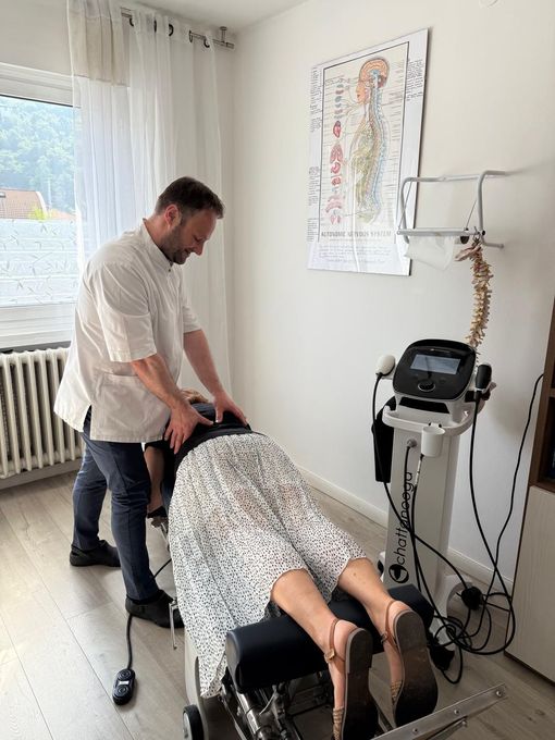 Chiropractor adjusting patient's spine; medical office setting. White coat, anatomy chart visible.