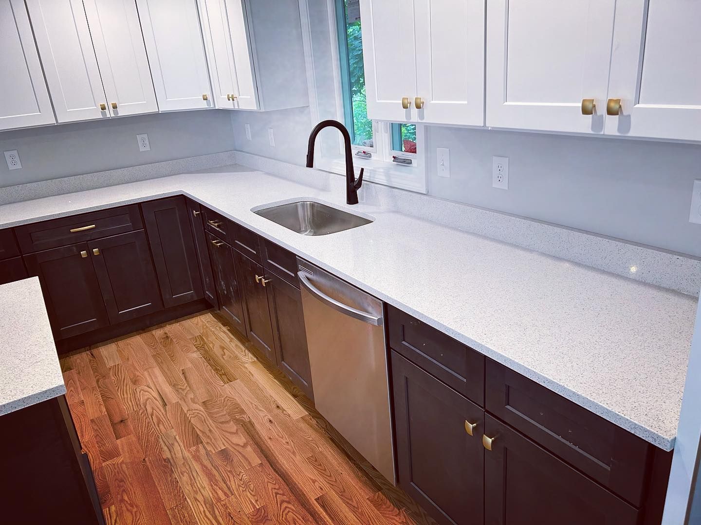 A kitchen with black cabinets , white counter tops , a sink and a dishwasher.