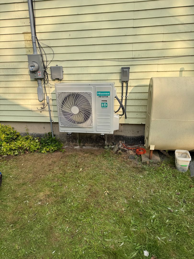 An air conditioning unit mounted on the wall of a building with grass in front.