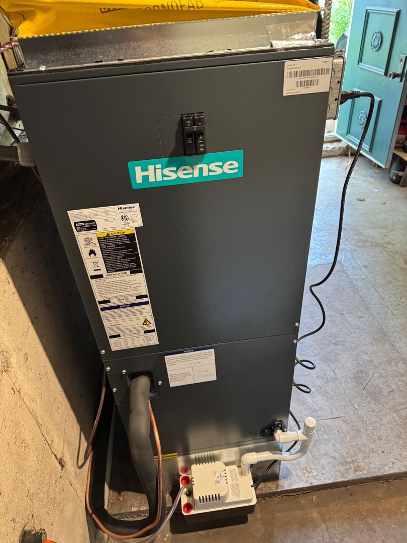 Hisense HVAC unit, gray with teal logo, electrical and coolant lines visible. Indoor setting.