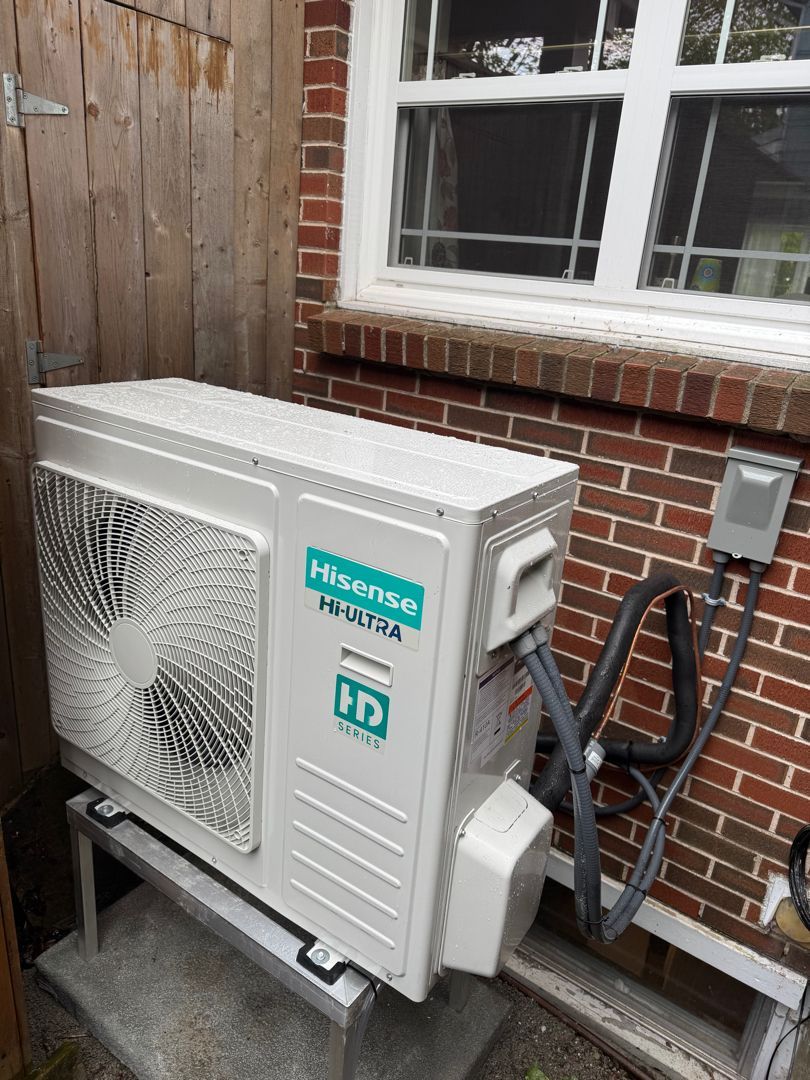 Hisense heat pump unit, outdoors, next to a brick wall and a wooden fence.