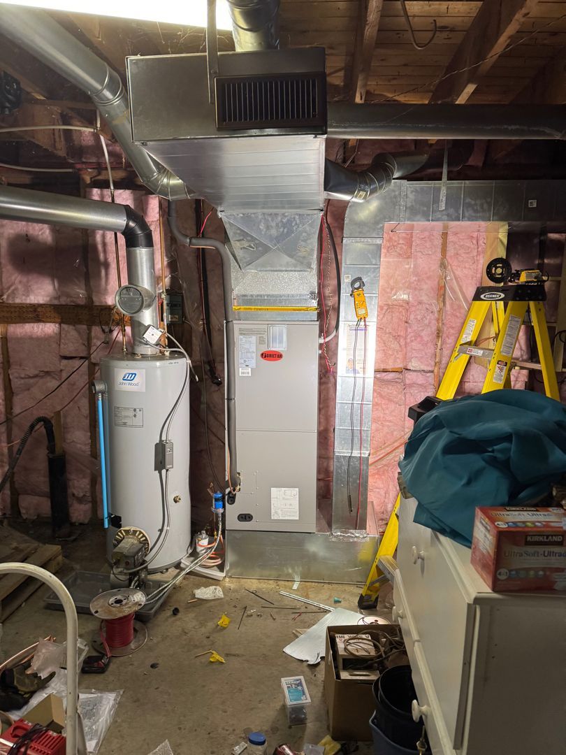 Furnace and water heater in a basement, surrounded by insulation and tools.