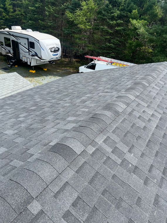 Gray shingle roof, RV, and utility truck in a wooded setting.