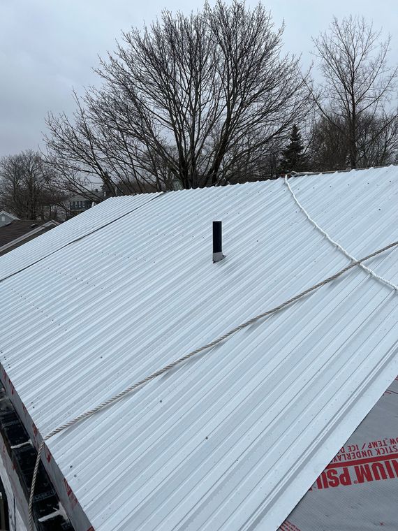 White corrugated metal roof with a vent pipe, overcast sky, tree in the background.