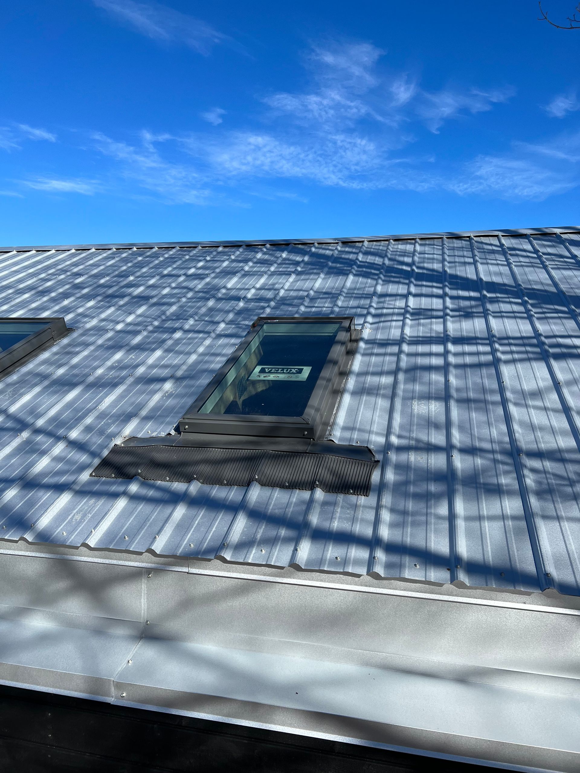 Metal roof with two skylights against a clear blue sky.