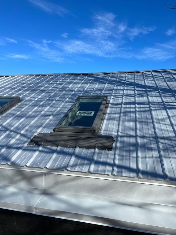 Metal roof with two skylights against a clear blue sky.