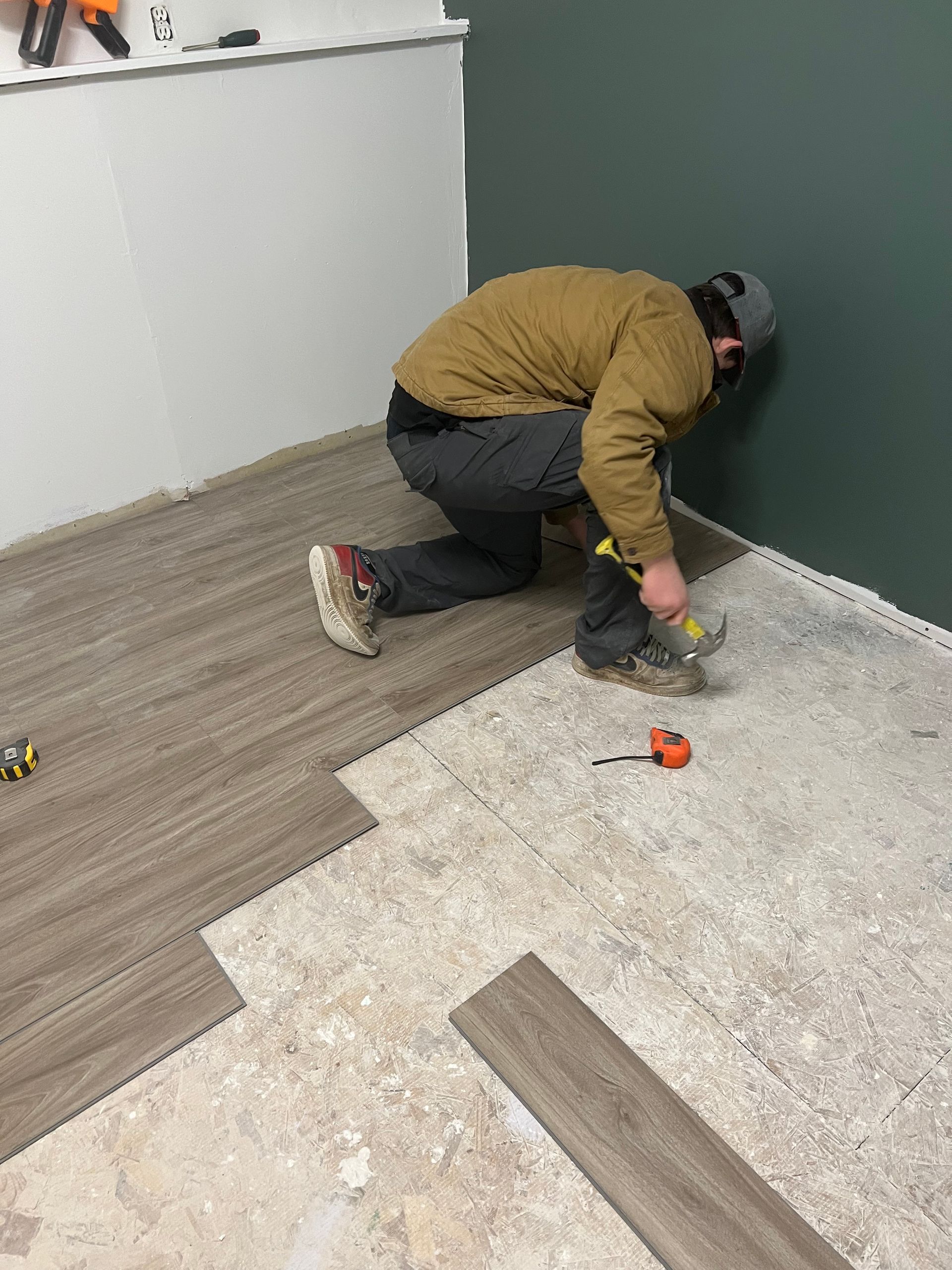 Man installing wood-look flooring on a concrete subfloor in a room with green and white walls.