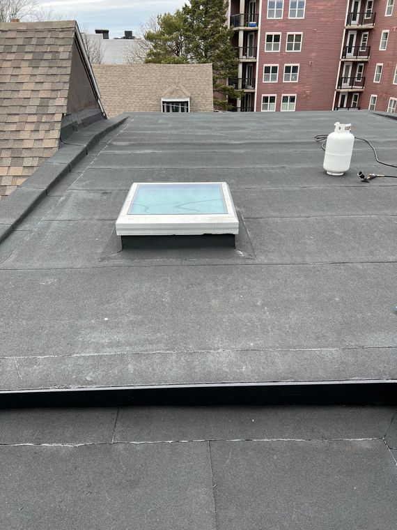 Flat rooftop with skylight, propane tank, and buildings in background.
