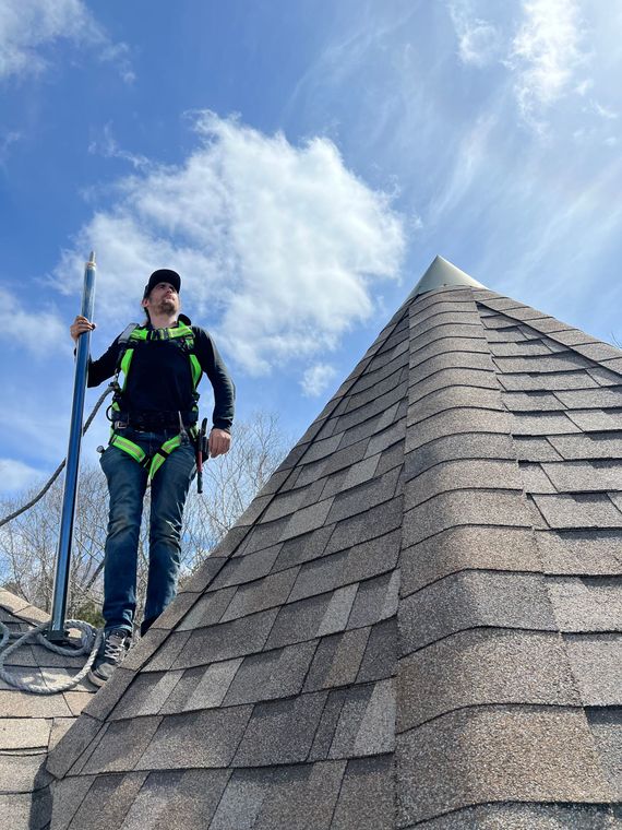 Man on pyramid roof with safety harness, holding tool. Blue sky with clouds.