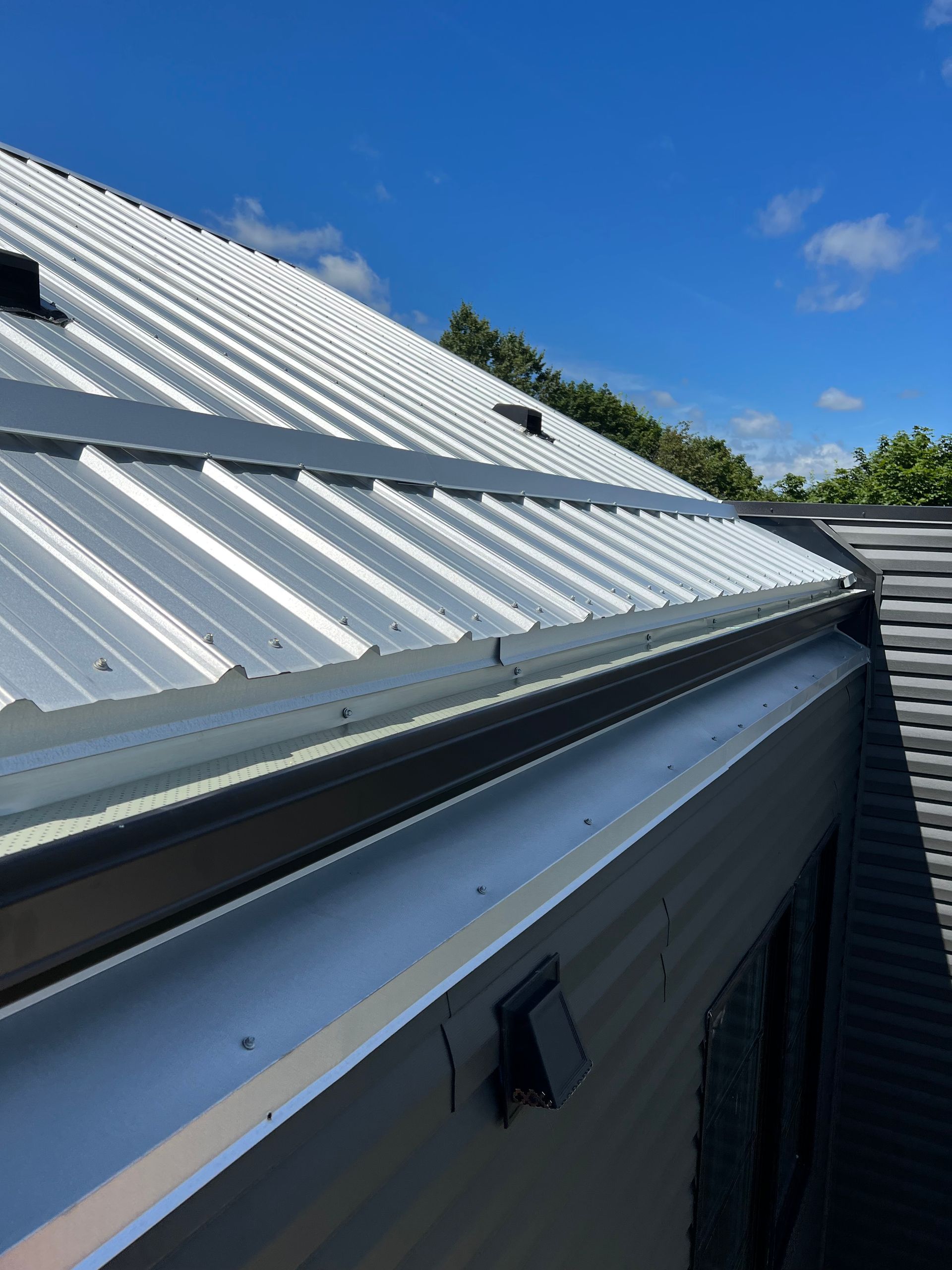 Silver metal roof with dark gray gutters against a blue sky.