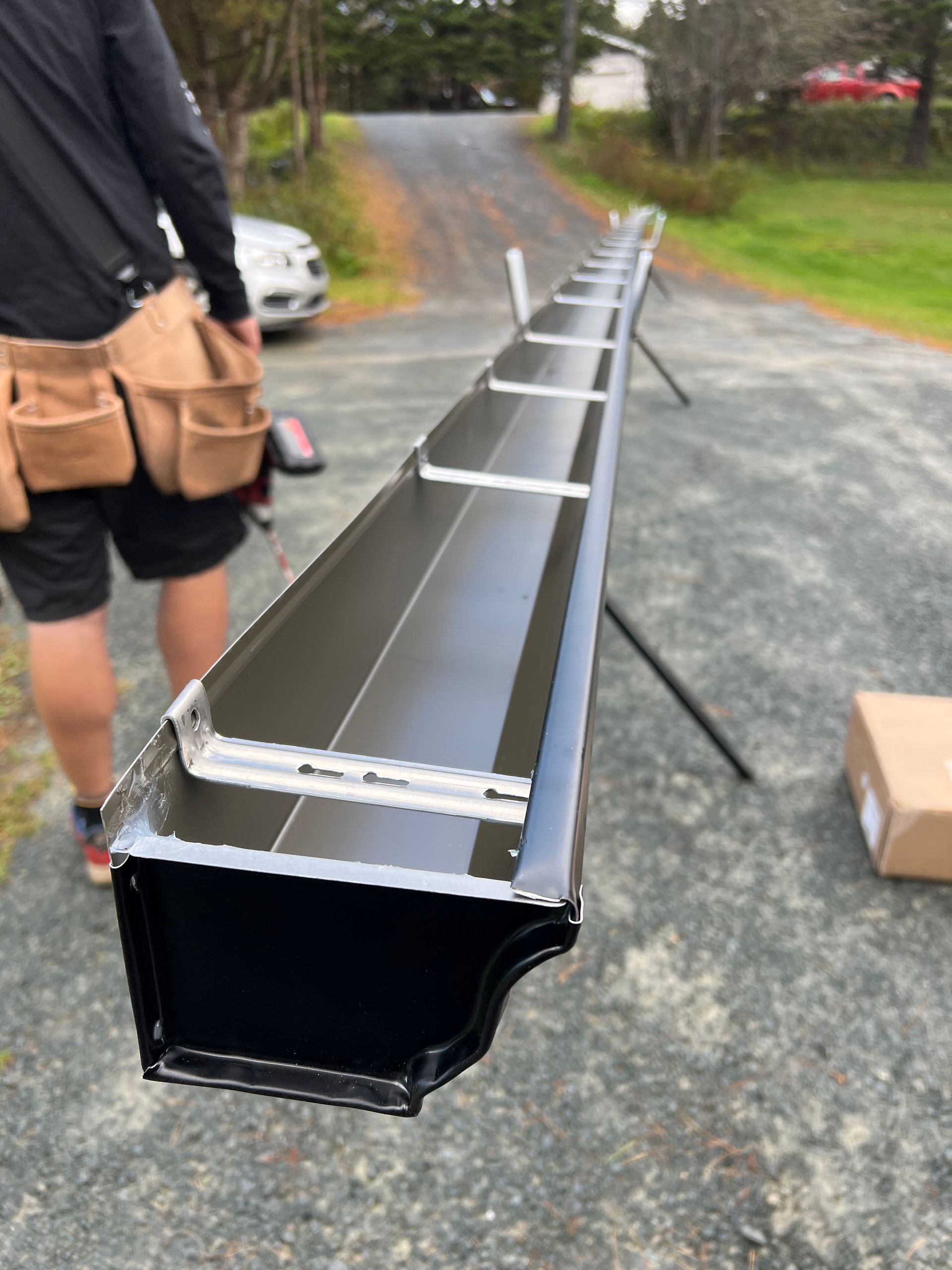 Man installing long black gutter on a driveway, outdoors.