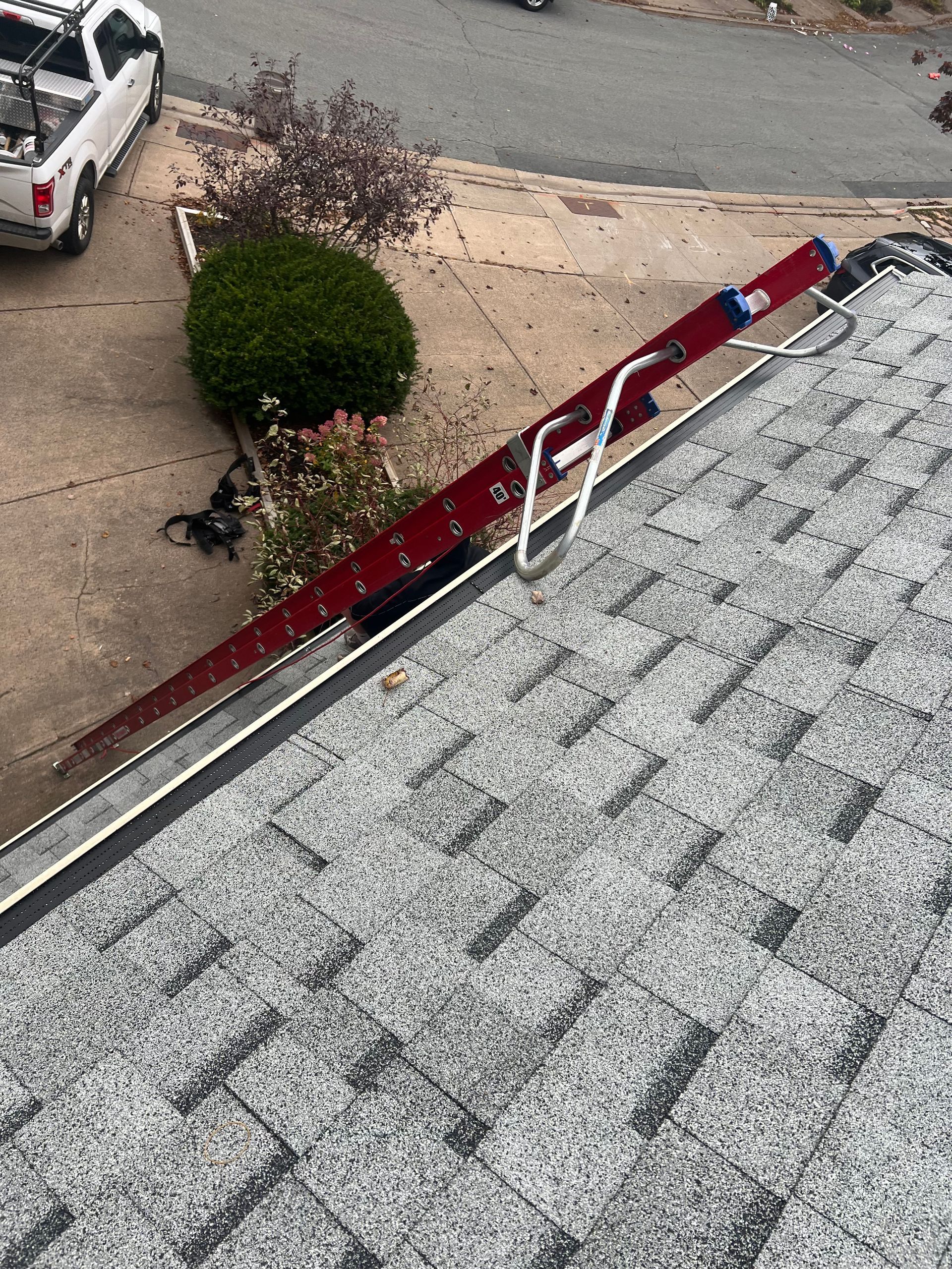 Red ladder secured to a roof gutter with a truck parked in the background.