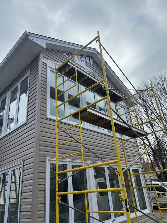 House exterior with tan siding and scaffolding, cloudy sky overhead.