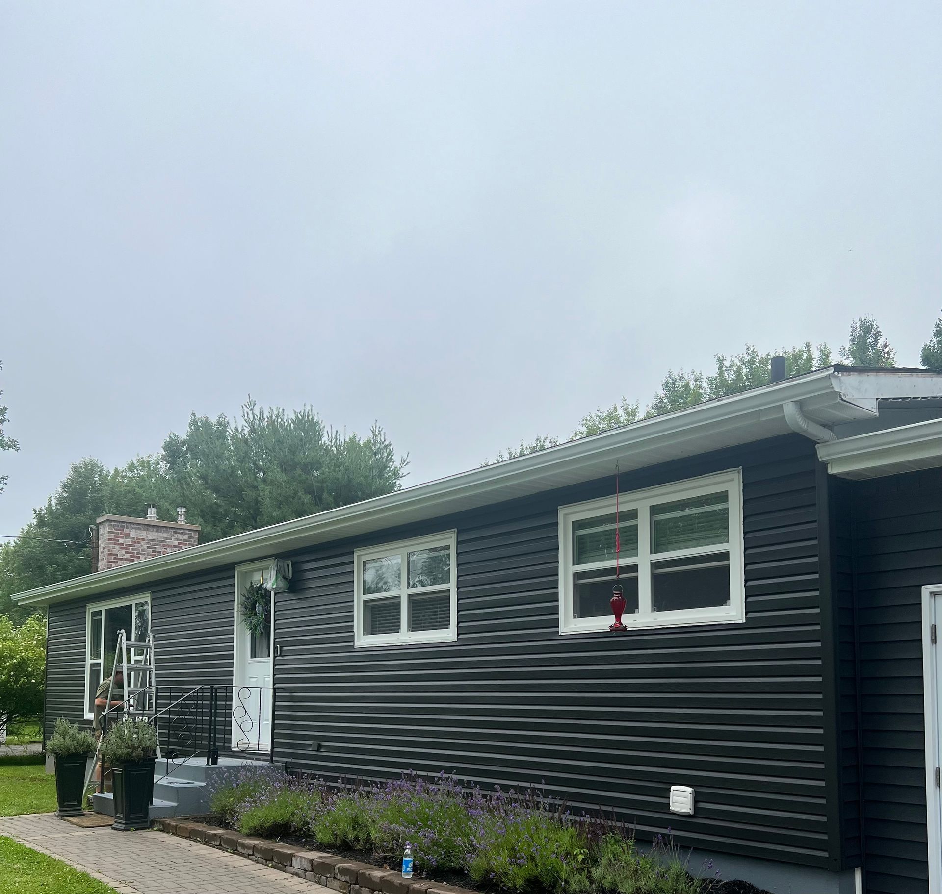 Black house with white trim, windows, and door, on a cloudy day. Landscaping in front.