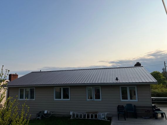 Tan house with a gray metal roof, several windows, and a blue sky.