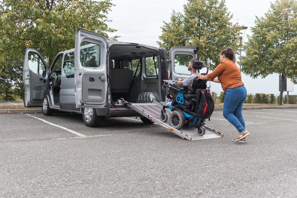 Person pushing wheelchair up ramp into gray van with open doors in parking lot
