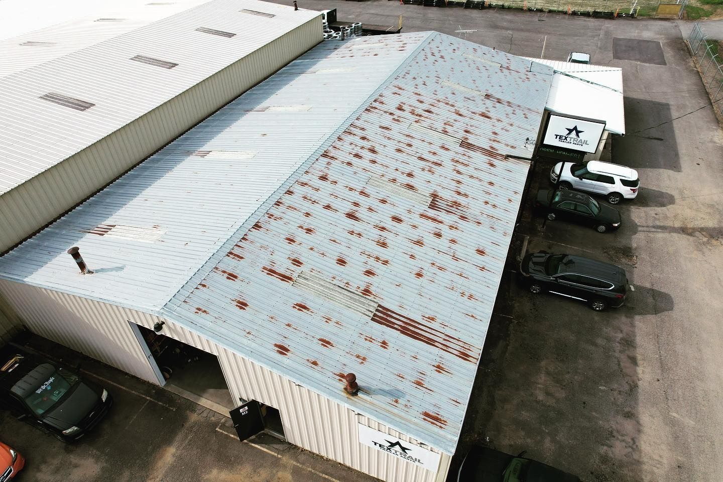 An aerial view of a building with a rusty roof and cars parked in front of it.