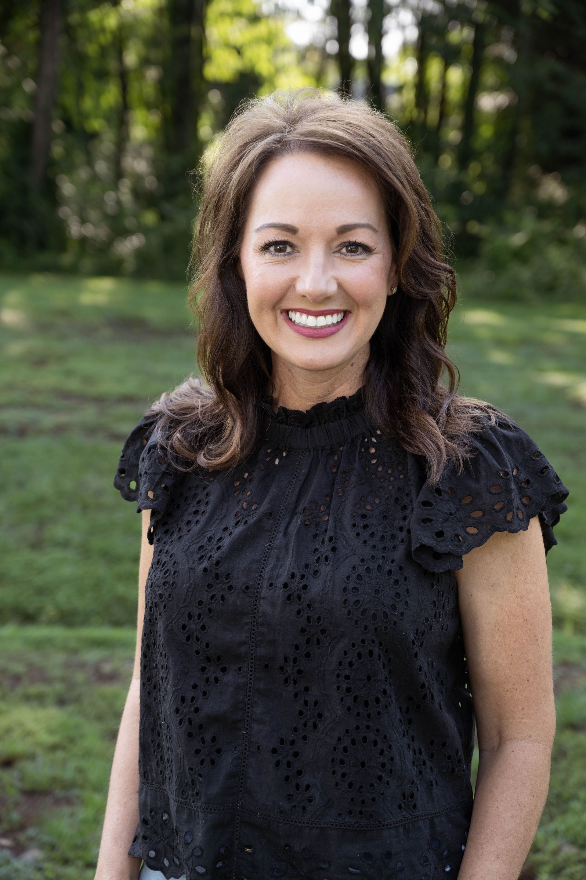 A woman in a black top is smiling for the camera while standing in the grass.