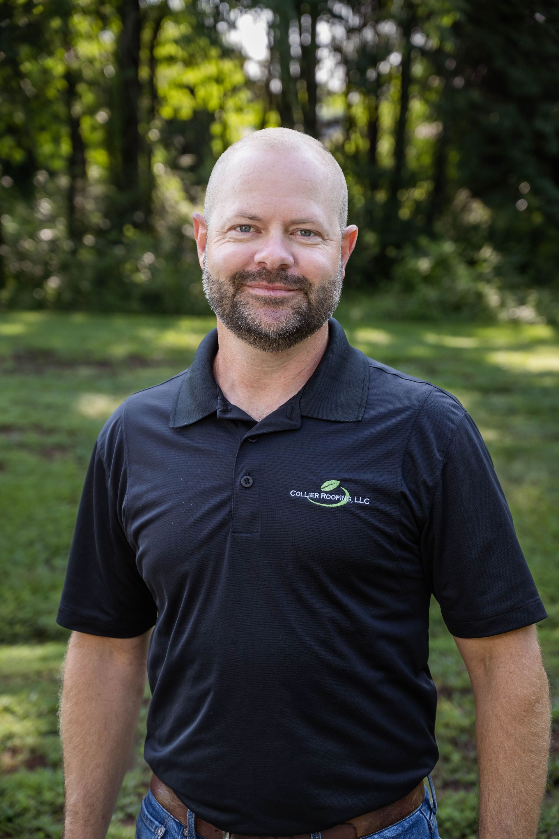 A man with a beard is wearing a black polo shirt and jeans.