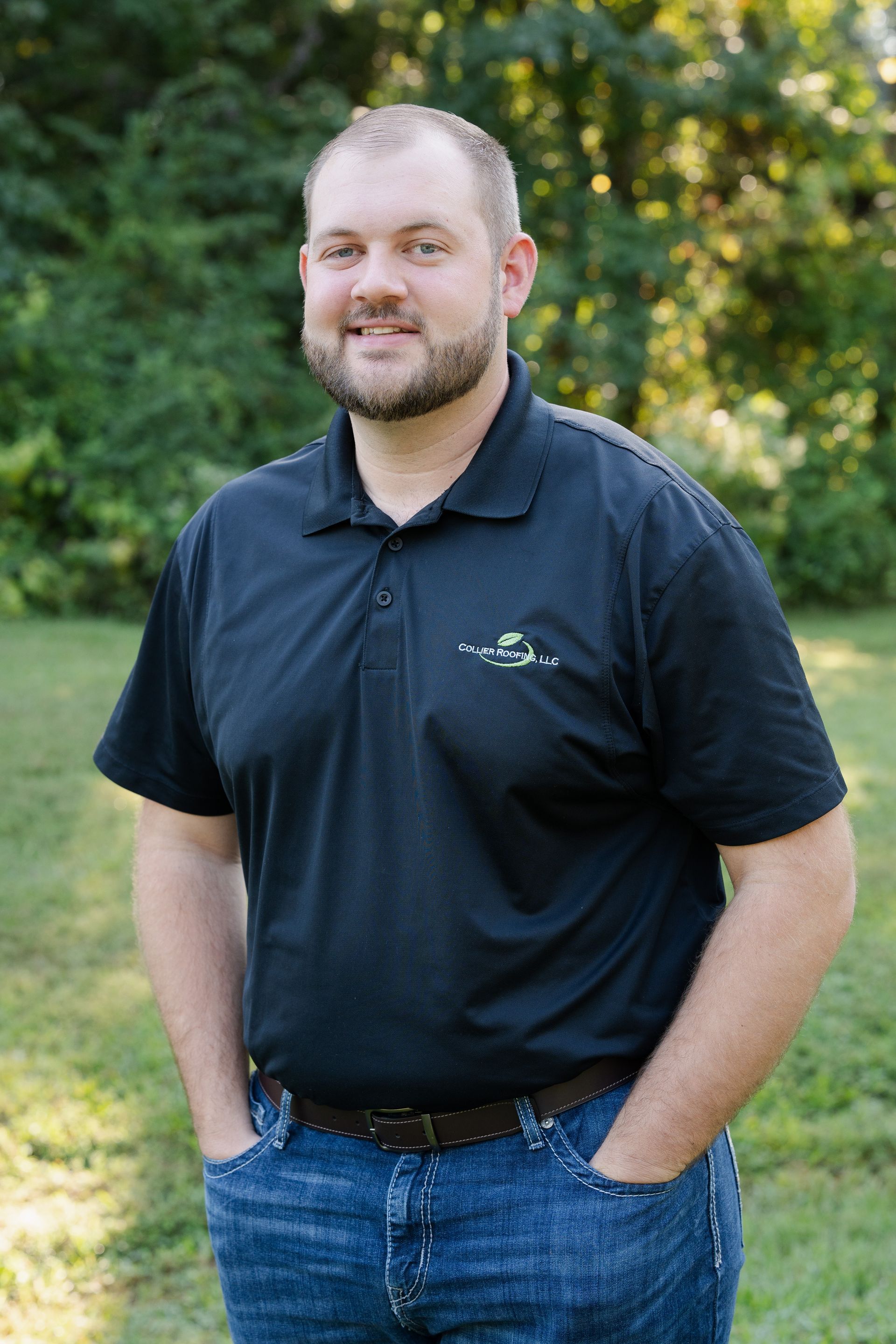 A man with a beard is standing in a field with his hands in his pockets.