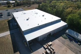 An aerial view of a large building with a white roof surrounded by trees.
