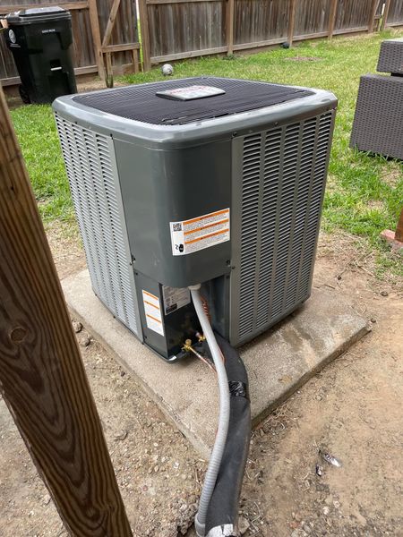 A large air conditioner is sitting on top of a concrete platform in a backyard.