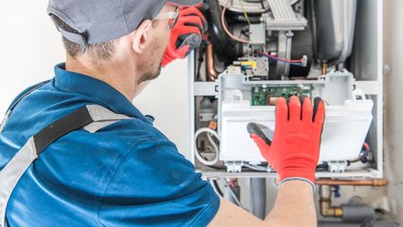 A man wearing red gloves is working on a boiler.