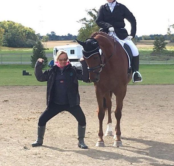 A trainer flexing her muscles beside a horse and rider at a dressage show