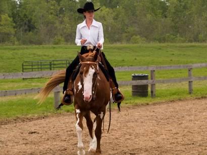 A trainer in a sand ring riding her horse western style