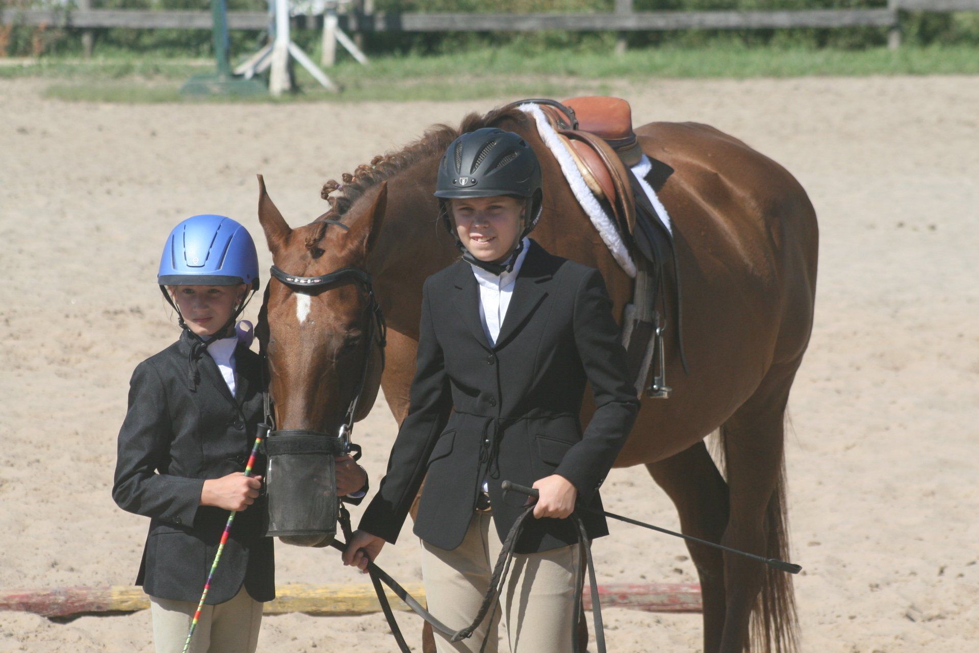 Two young riders holding horse in sand ring