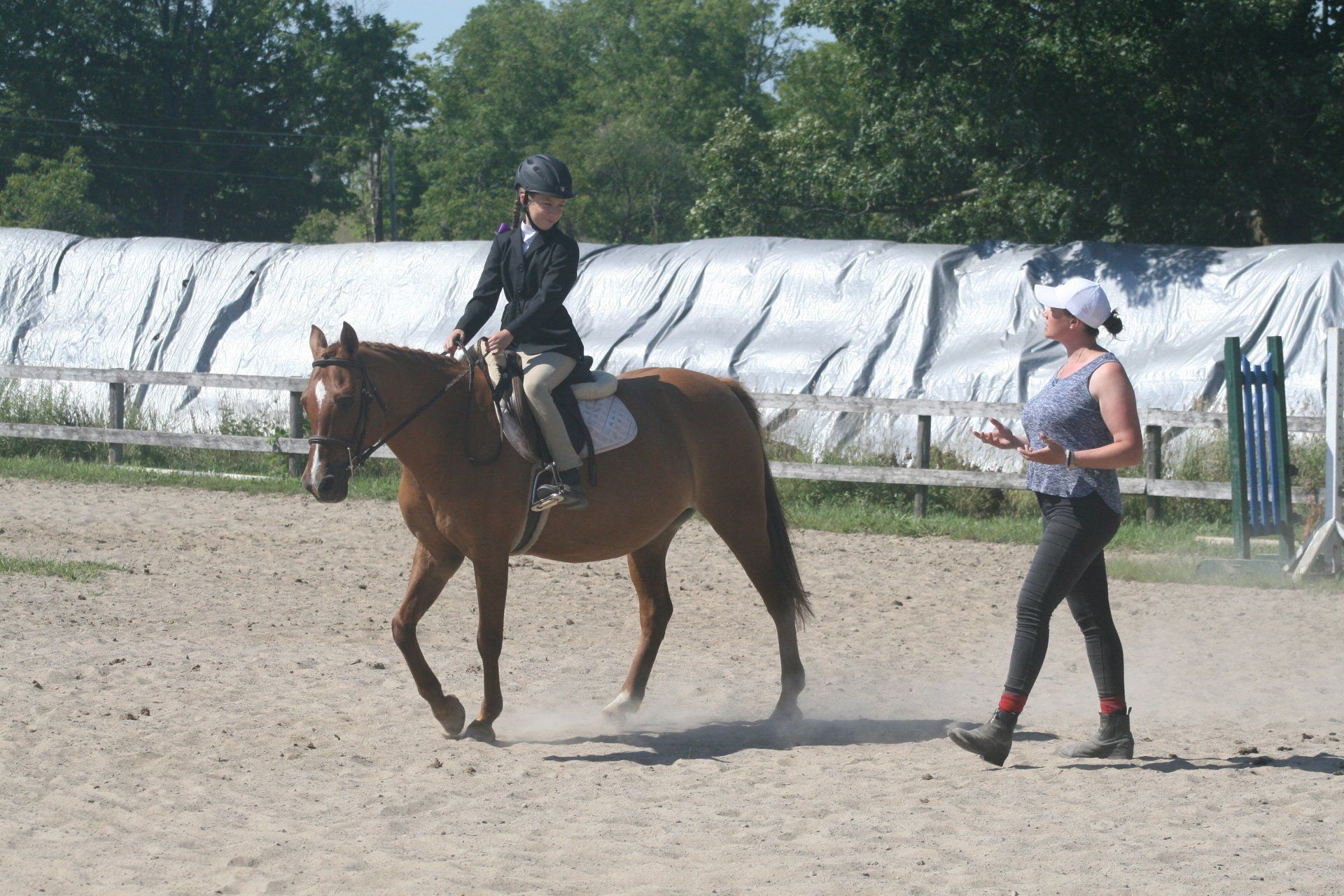 Coach instructing young rider on horse in sand ring
