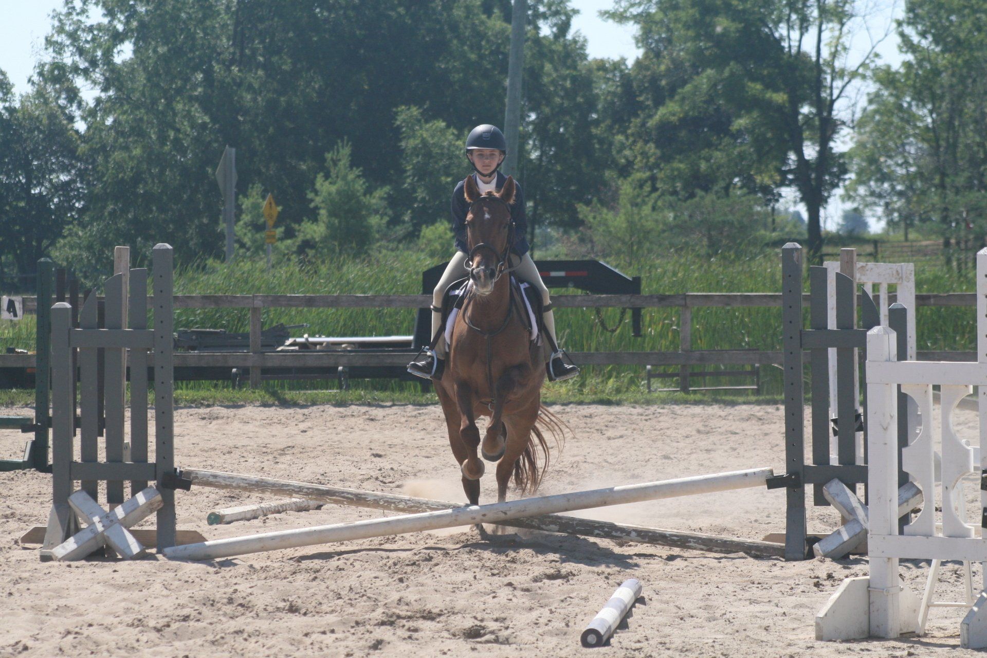 Young rider on pony jumping a cross rail in sand ring