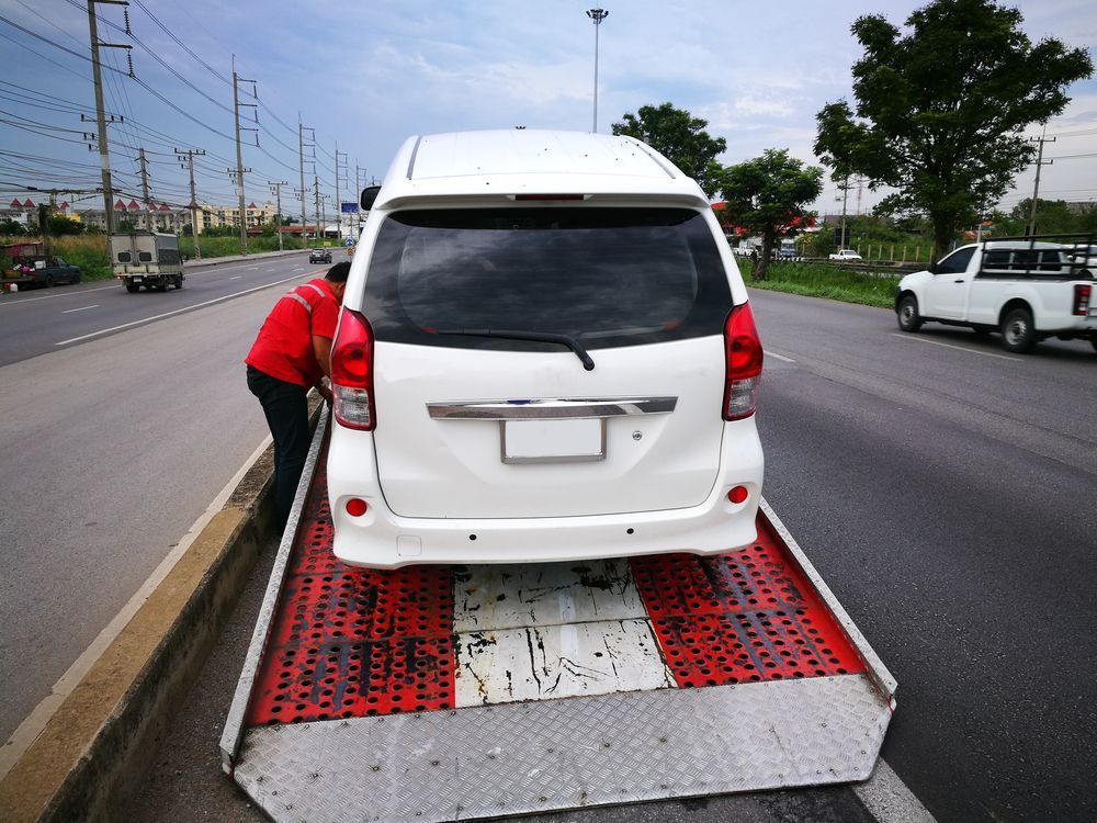 White Minivan Being Towed onto A Flatbed Tow Truck on The Side of A Road — Sundance Auto & Machinery Pty Ltd In Mackay, QLD